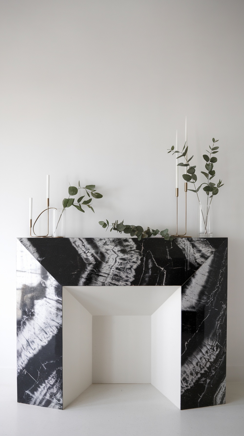 A modern minimalist mantelpiece with a black and white design, featuring candles and greenery.