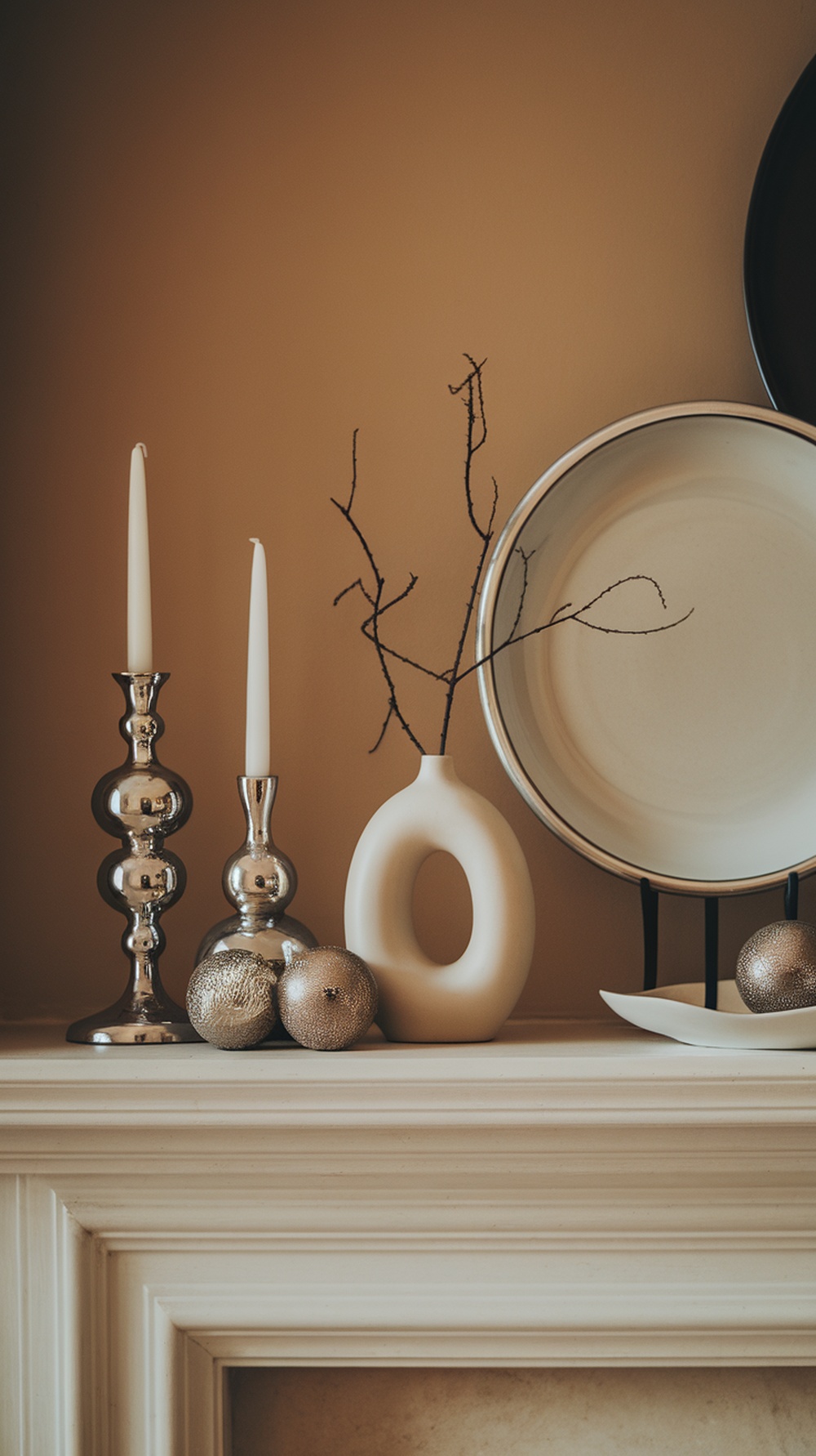 A minimalist winter mantle decor featuring silver candlesticks, a white vase, and silver ornaments.