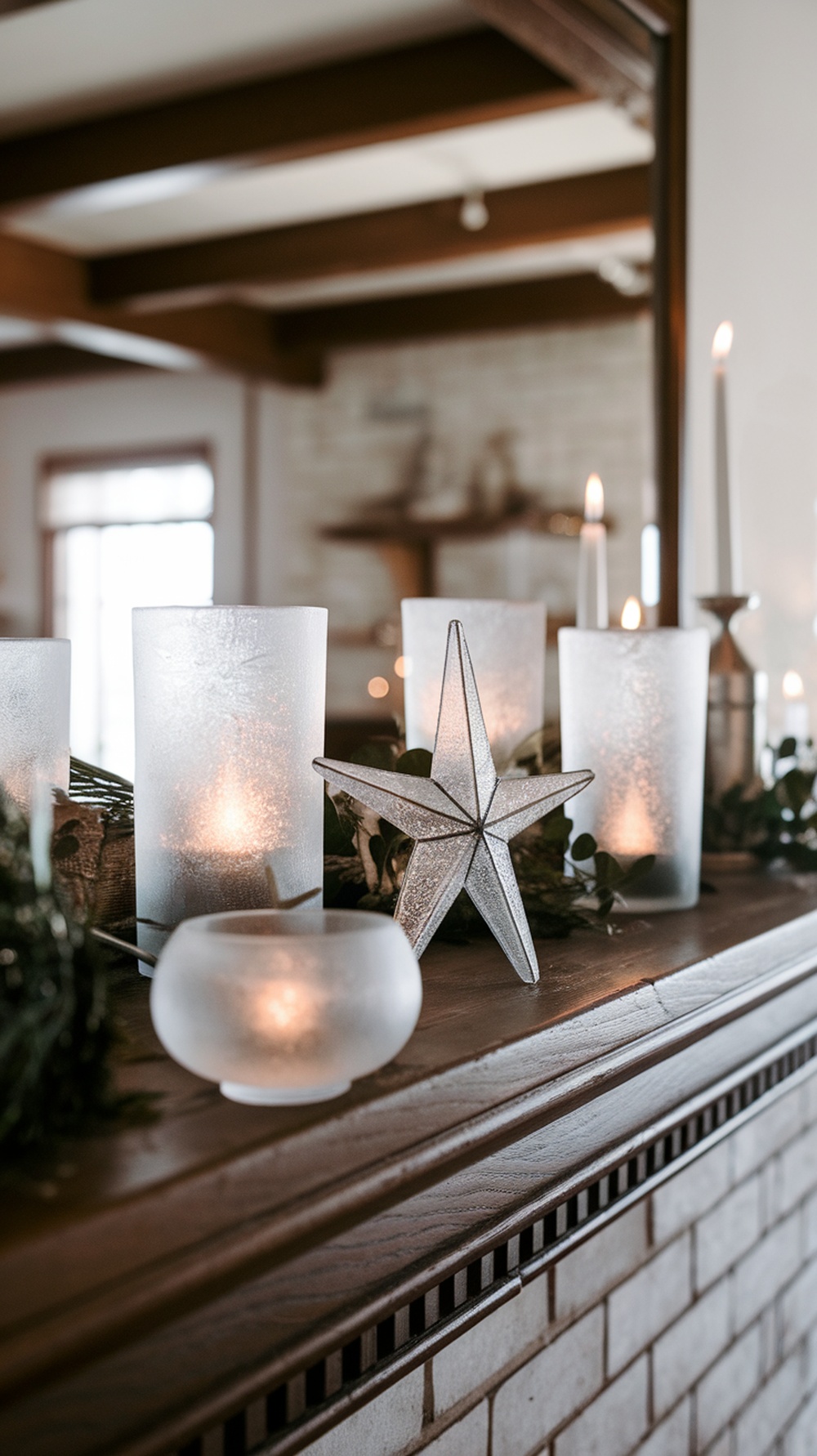 A winter mantle decor featuring frosted glass candle holders, a silver star decoration, and greenery.