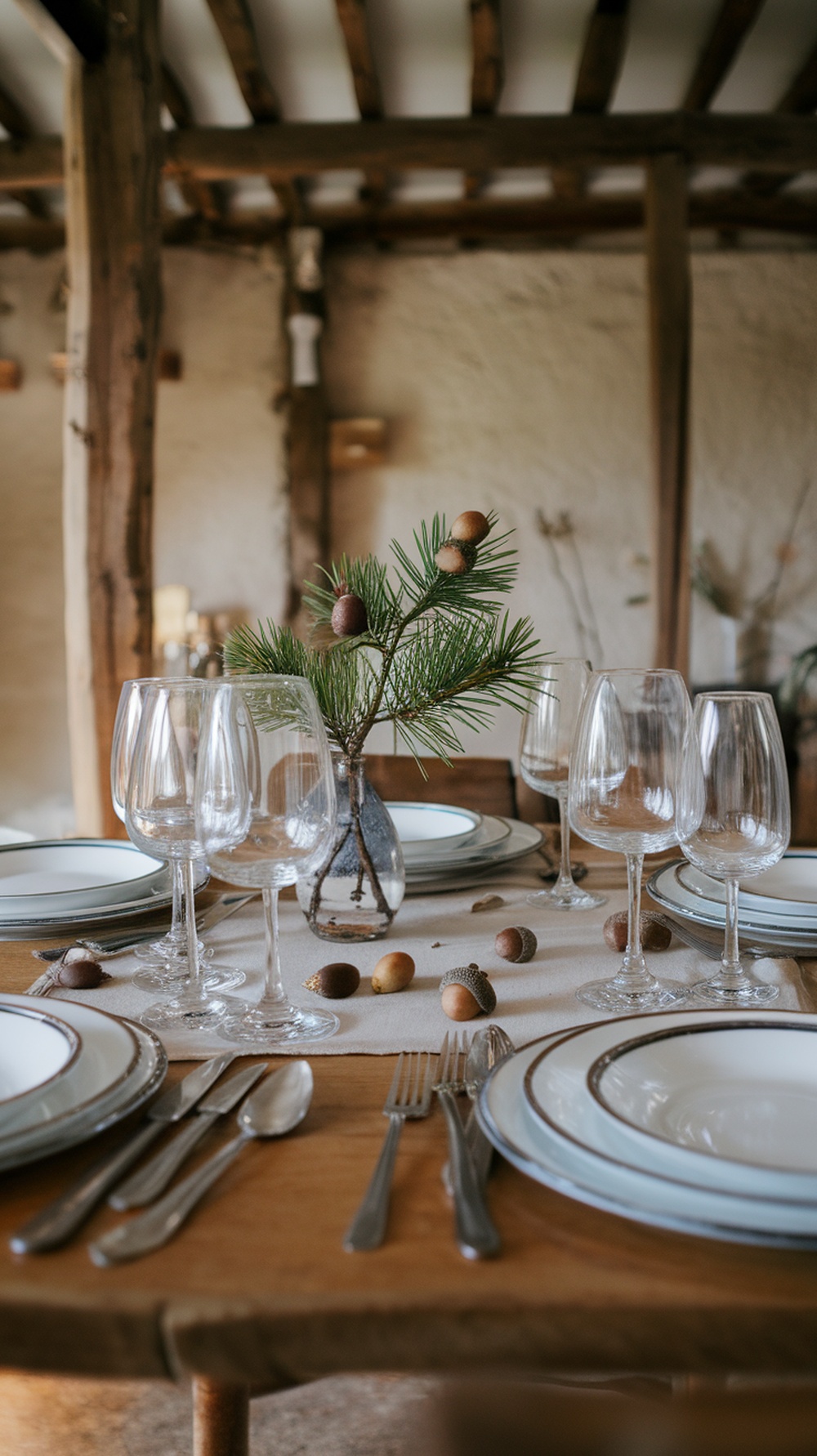 A rustic table setting featuring a centerpiece of pine branches and acorns, with elegant glassware and plates.